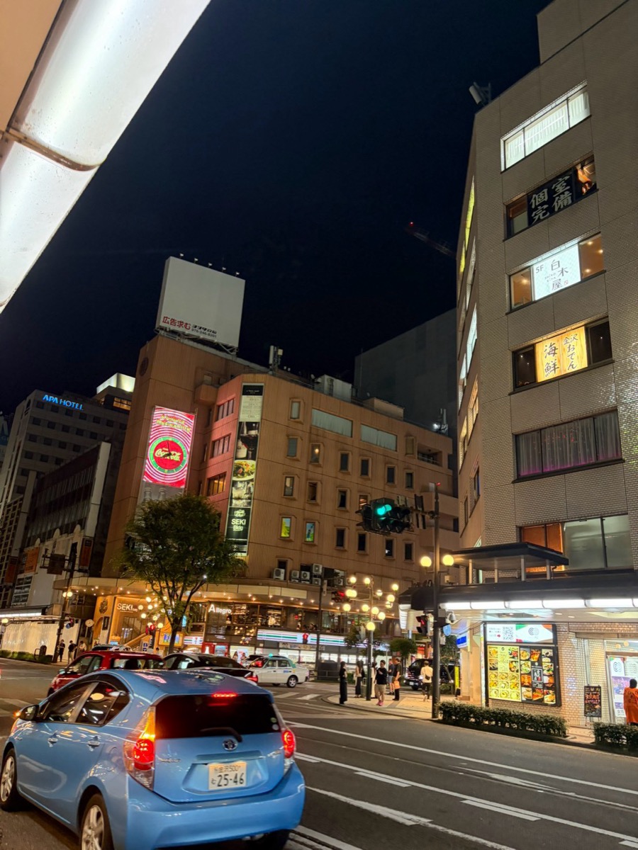 夜の片町交差点。四方のビルに明かりが灯り、車と人が行き交っている
